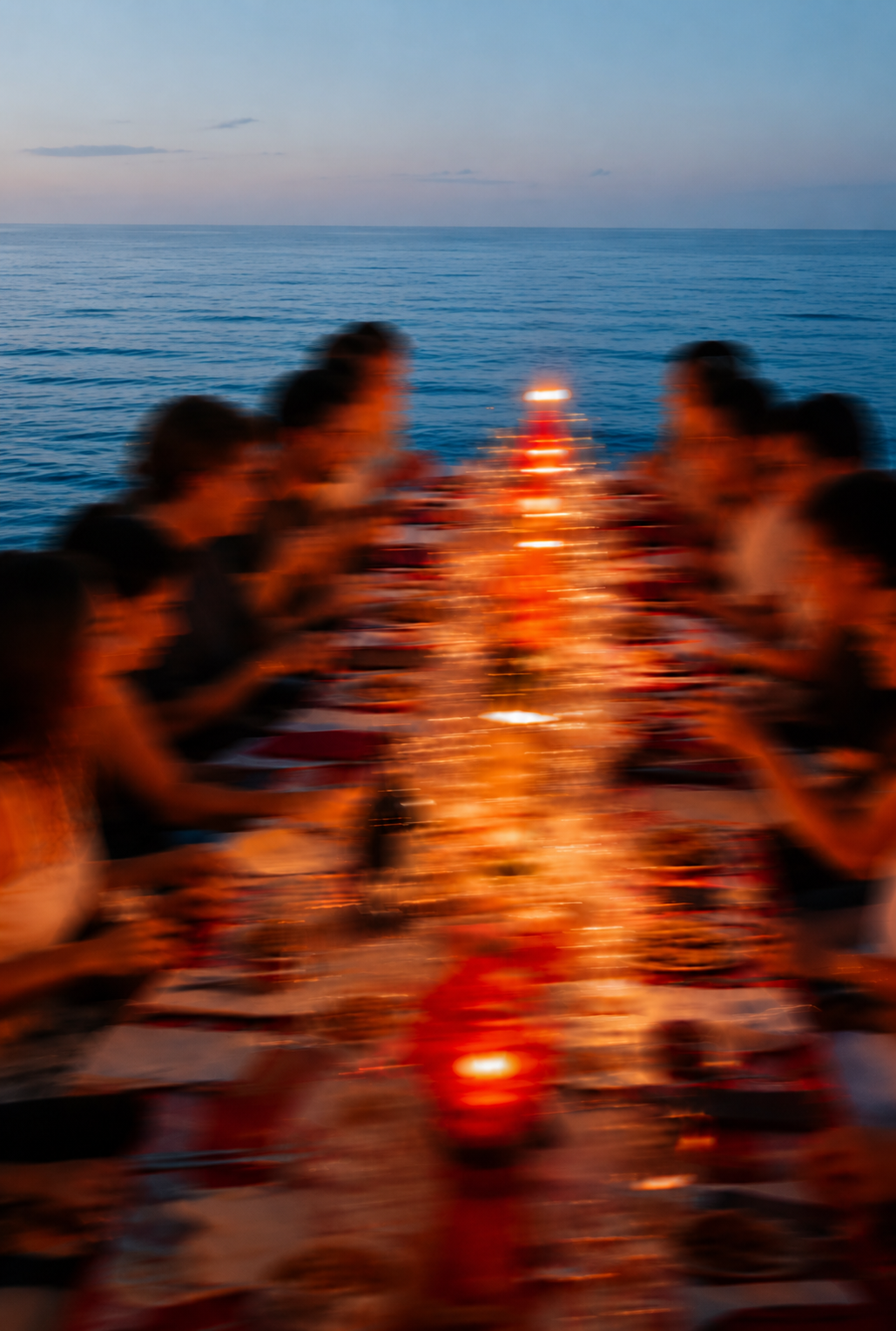 A long communal table at dusk, lit with candles and captured in motion blur
